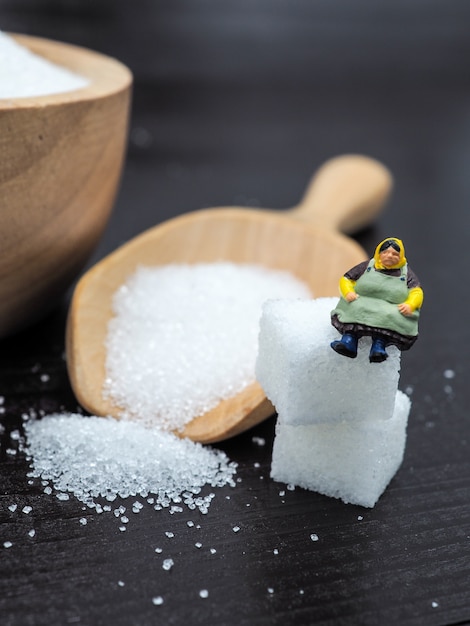 Donna grassa miniatura vicino alla ciotola di legno con il cubo di zucchero su fondo di legno scuro.