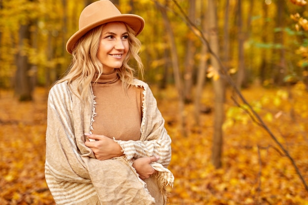 Donna graziosa alla moda che cammina all'aperto nel parco o nella foresta di primavera autunno