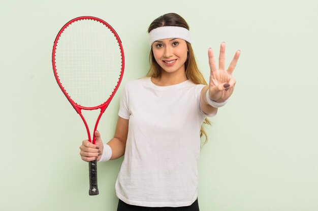 Donna graziosa asiatica che sorride e che sembra amichevole, mostrando il numero tre. concetto di tennis