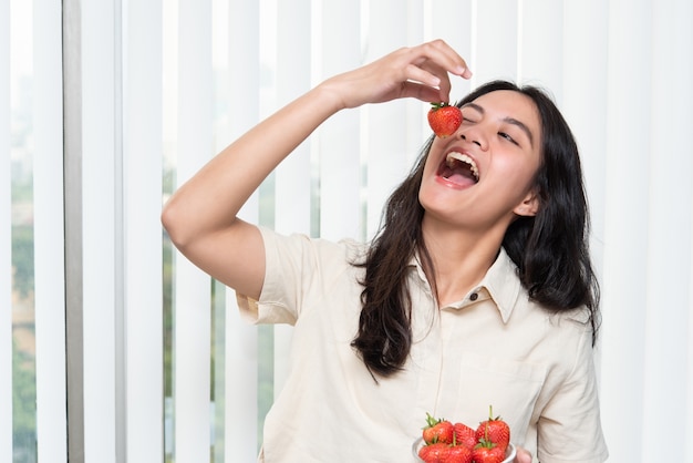 Donna graziosa asiatica che tiene e che mangia fragole fresche