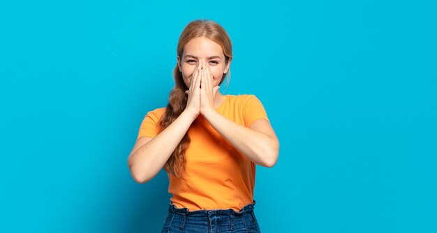 Donna graziosa bionda che sembra bocca della copertura felice, allegra, fortunata e sorpresa con entrambe le mani