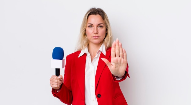 Donna graziosa bionda che sembra seria mostrando il palmo aperto facendo il gesto di arresto preporter e il concetto di microfono