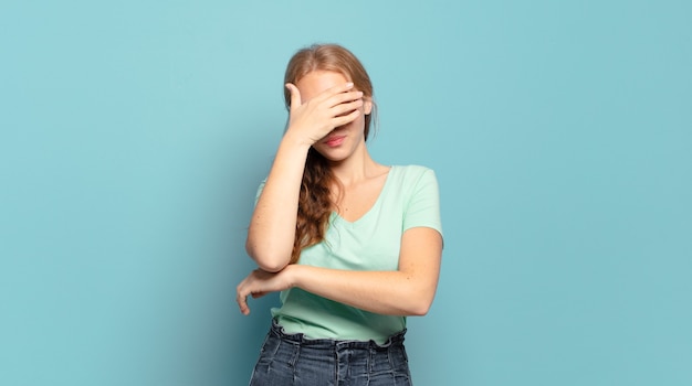 Donna graziosa bionda che sembra stressata, vergognosa o turbata, con un mal di testa, che copre il viso con la mano