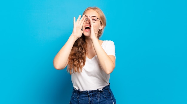 Donna graziosa bionda che si sente felice, eccitata e positiva, dando un grande grido con le mani vicino alla bocca, chiamando