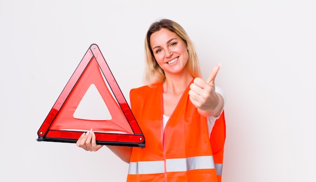 Donna graziosa bionda che si sente orgogliosa di sorridere positivamente con i pollici in su concetto di incidente del triangolo dell'auto