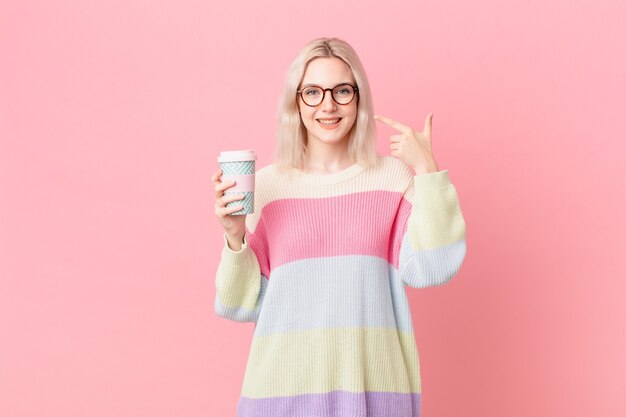 Donna graziosa bionda che sorride con sicurezza indicando il proprio ampio sorriso. concetto di caffè