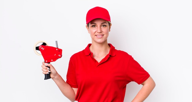 Donna graziosa bionda che sorride felicemente con una mano sull'anca e concetto di lavoratore fiducioso