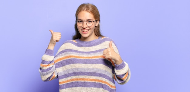 Donna graziosa bionda che sorride largamente felice, positiva, sicura e di successo, con entrambi i pollici in su