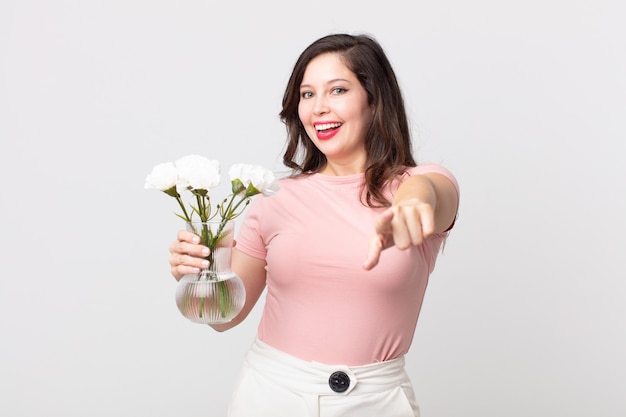 Donna graziosa che indica la macchina fotografica che ti sceglie e che tiene un vaso di fiori decorativo