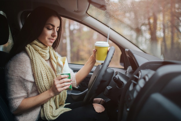 Donna graziosa che mangia alimento e che guida in sua automobile