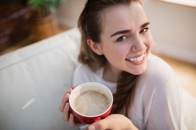 Donna graziosa che si distende sullo strato con caffè nel salone