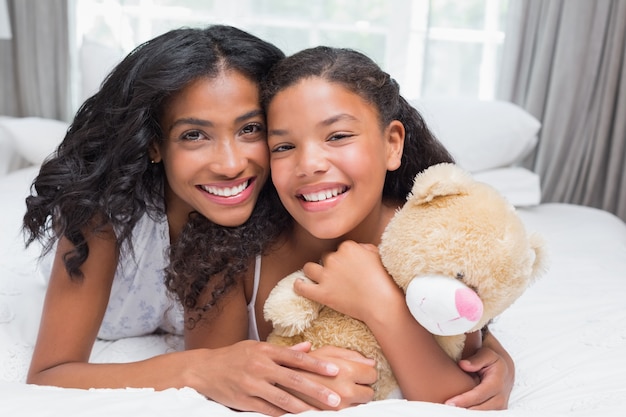 Donna graziosa che si trova sul letto con sua figlia che sorride alla macchina fotografica