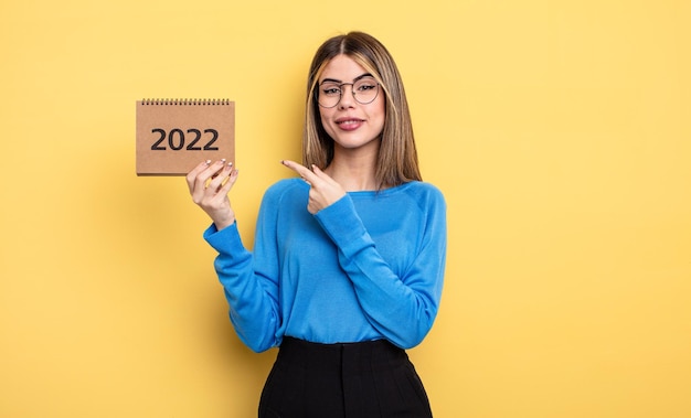 Donna graziosa che sorride allegramente sentendosi felice e indicando il concetto di calendario 2022 laterale