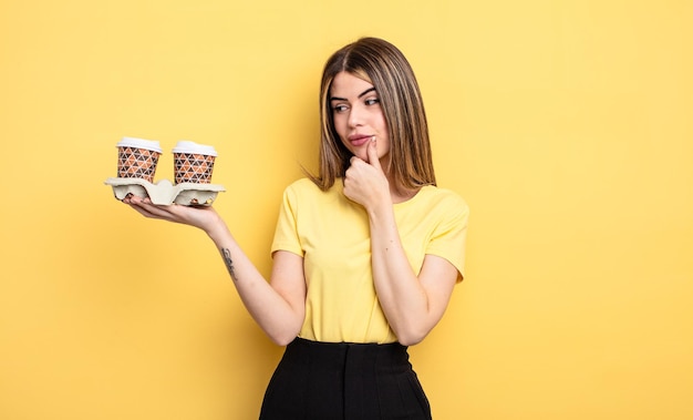 Donna graziosa che sorride con un'espressione felice e sicura con la mano sul mento. concetto di caffè da asporto