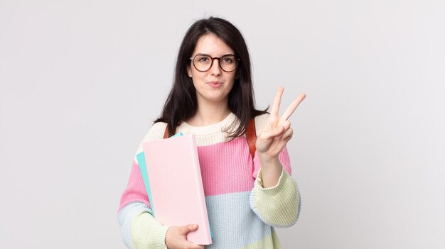 Donna graziosa che sorride e che sembra amichevole, mostrando il numero due. concetto di studente universitario