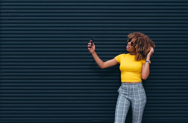 Donna graziosa con i capelli afro che per mezzo del telefono cellulare.