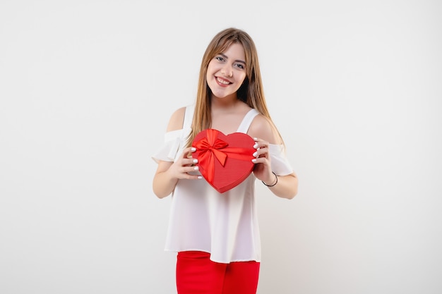 Donna graziosa con il contenitore di regalo del biglietto di S. Valentino a forma di cuore rosso isolato