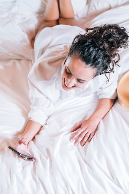 Donna graziosa con il telefono a letto