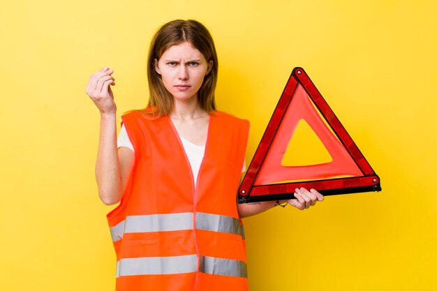 Donna graziosa con la testa rossa che fa un gesto di capice o denaro che ti dice di pagare il pericolo del triangre dell'auto