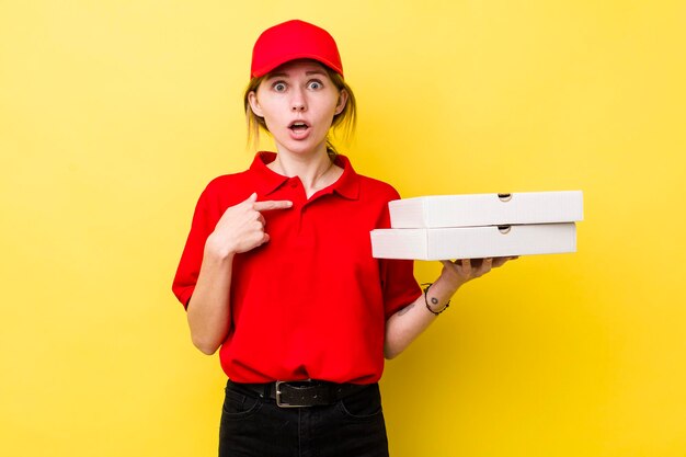 Donna graziosa con la testa rossa che sembra scioccata e sorpresa con la bocca spalancata che punta al concetto di pizza con consegna automatica