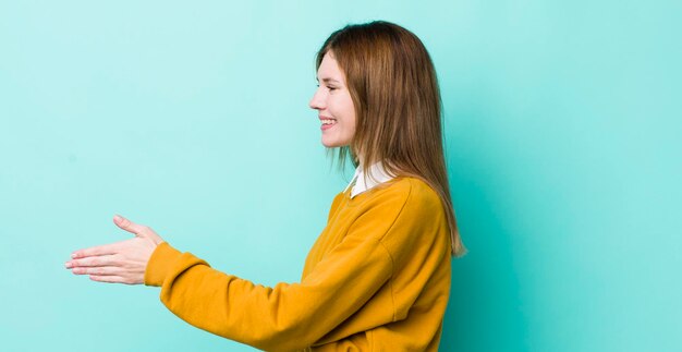 Donna graziosa con la testa rossa che sorride salutandoti e offrendoti una stretta di mano per chiudere un concetto di cooperazione di successo