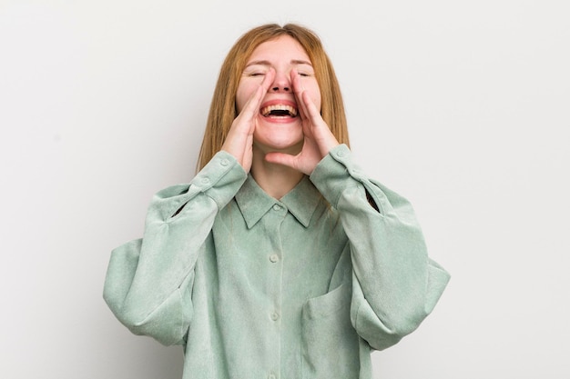 Donna graziosa dalla testa rossa che si sente felice eccitata e positiva dando un grande grido con le mani accanto alla bocca che gridano