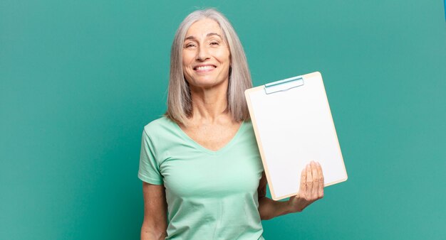 Donna graziosa dei capelli grigi che mostra un pezzo di carta vuoto