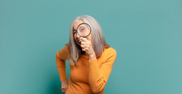 Donna graziosa dei capelli grigi con una lente d'ingrandimento