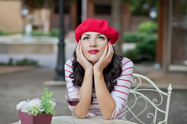 Donna graziosa del brunette in una maglietta a strisce che beve vino rosso in caffè esterno.