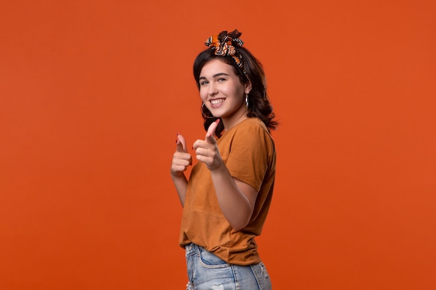 Donna graziosa del brunette in una maglietta e nella bella fascia che indica con le sue dita alla macchina fotografica. Posto per l'annuncio.