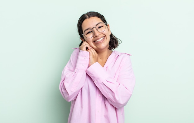 Donna graziosa dell'adolescente che si sente innamorata e sembra carina, adorabile e felice, sorridente romanticamente con le mani accanto al viso