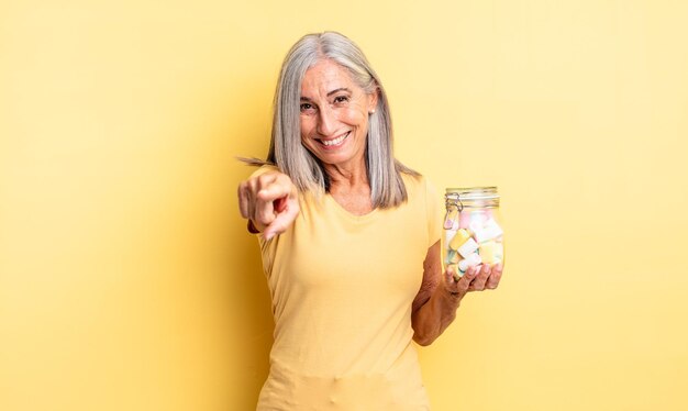 Donna graziosa di mezza età che indica alla macchina fotografica che ti sceglie. concetto di bottiglia di caramelle