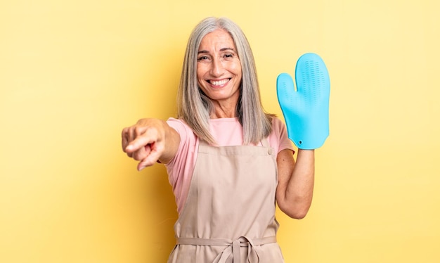 Donna graziosa di mezza età che indica alla macchina fotografica che ti sceglie. concetto di guanto da forno