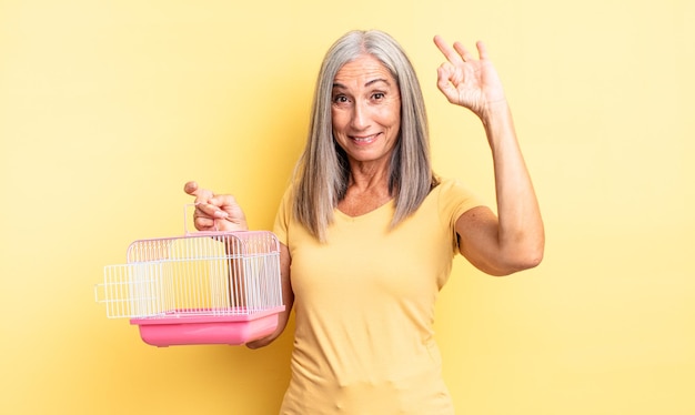 Donna graziosa di mezza età che si sente felice, mostrando approvazione con un gesto ok. concetto di gabbia o prigione per animali domestici