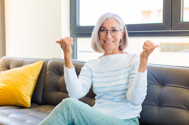 Donna graziosa di mezza età che sorride con gioia e sembra felice, sentendosi spensierata e positiva con entrambi i pollici in su