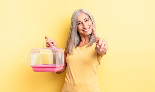 Donna graziosa di mezza età che sorride con orgoglio e sicurezza facendo il numero uno. concetto di gabbia o prigione per animali domestici