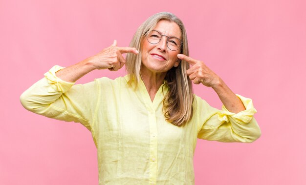 Donna graziosa di mezza età con camicia gialla e occhiali da vista sull'azzurro