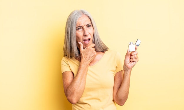 Donna graziosa di mezza età con la bocca e gli occhi spalancati e la mano sul mento. concetto più leggero