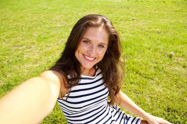 Donna graziosa felice che prende la foto del selfie su erba