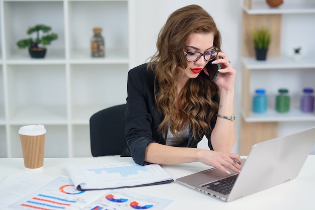 Donna graziosa in vetri che ha conversazione telefonica di affari