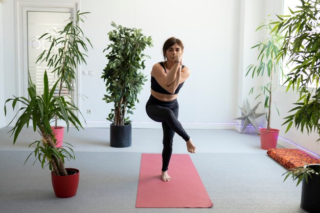 Donna graziosa matura che indossa abiti sportivi che praticano le pose di yoga