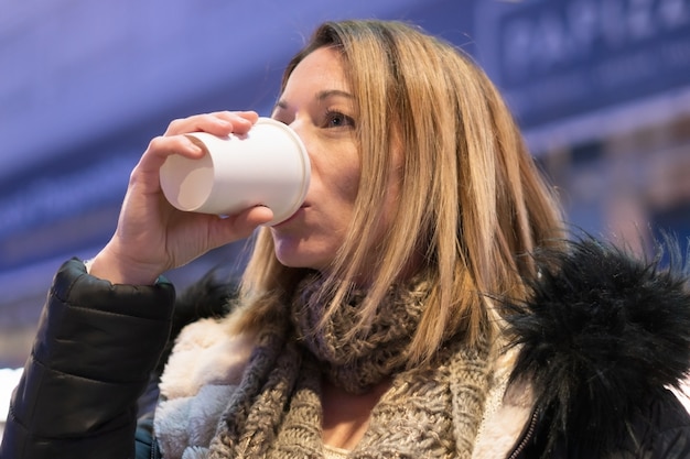 Donna graziosa nella città di notte che beve caffè. Sfondo di luci della città.