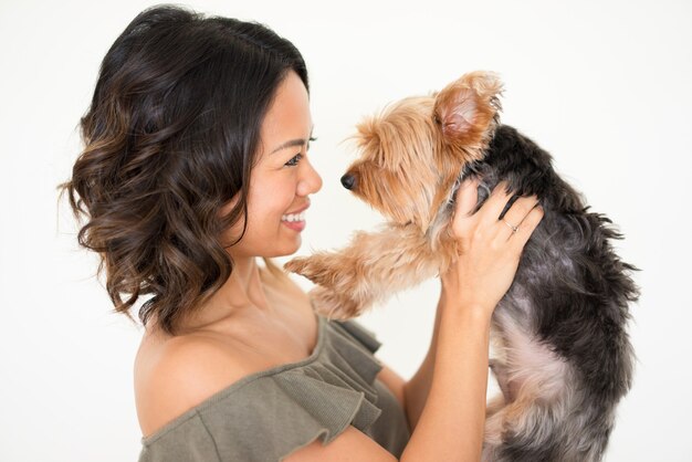 Donna graziosa sorridente che alza Yorkshire terrier