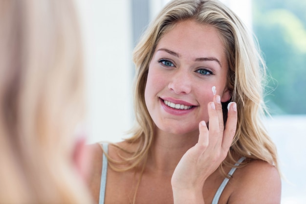 Donna graziosa sorridente che applica crema sul suo fronte in bagno