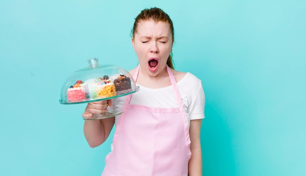 Donna graziosa testa rossa che grida in modo aggressivo concetto di torte fatte in casa molto arrabbiato