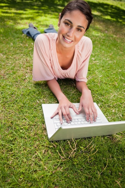 Donna guardando avanti mentre si utilizza un computer portatile come lei si sdraia nell&#39;erba