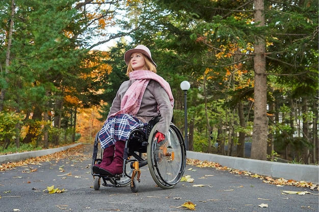 Donna handicappata paralizzata su sedia a rotelle si muove nel parco d'autunno