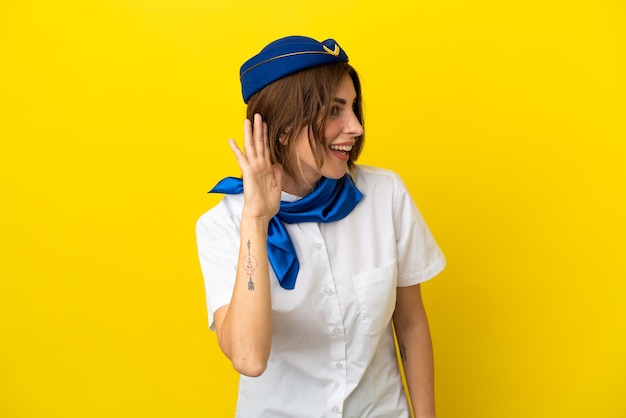 Donna hostess aeroplano isolata su sfondo giallo ascoltando qualcosa mettendo la mano sull'orecchio