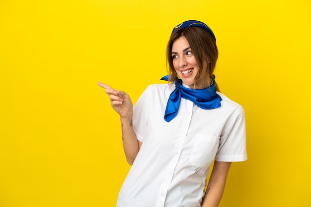 Donna hostess aeroplano isolata su sfondo giallo che punta il dito sul lato e presenta un prodotto