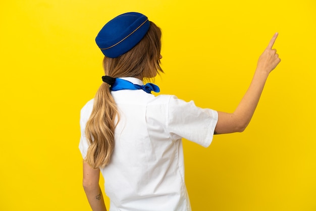 Donna hostess aeroplano isolata su sfondo giallo che punta indietro con il dito indice